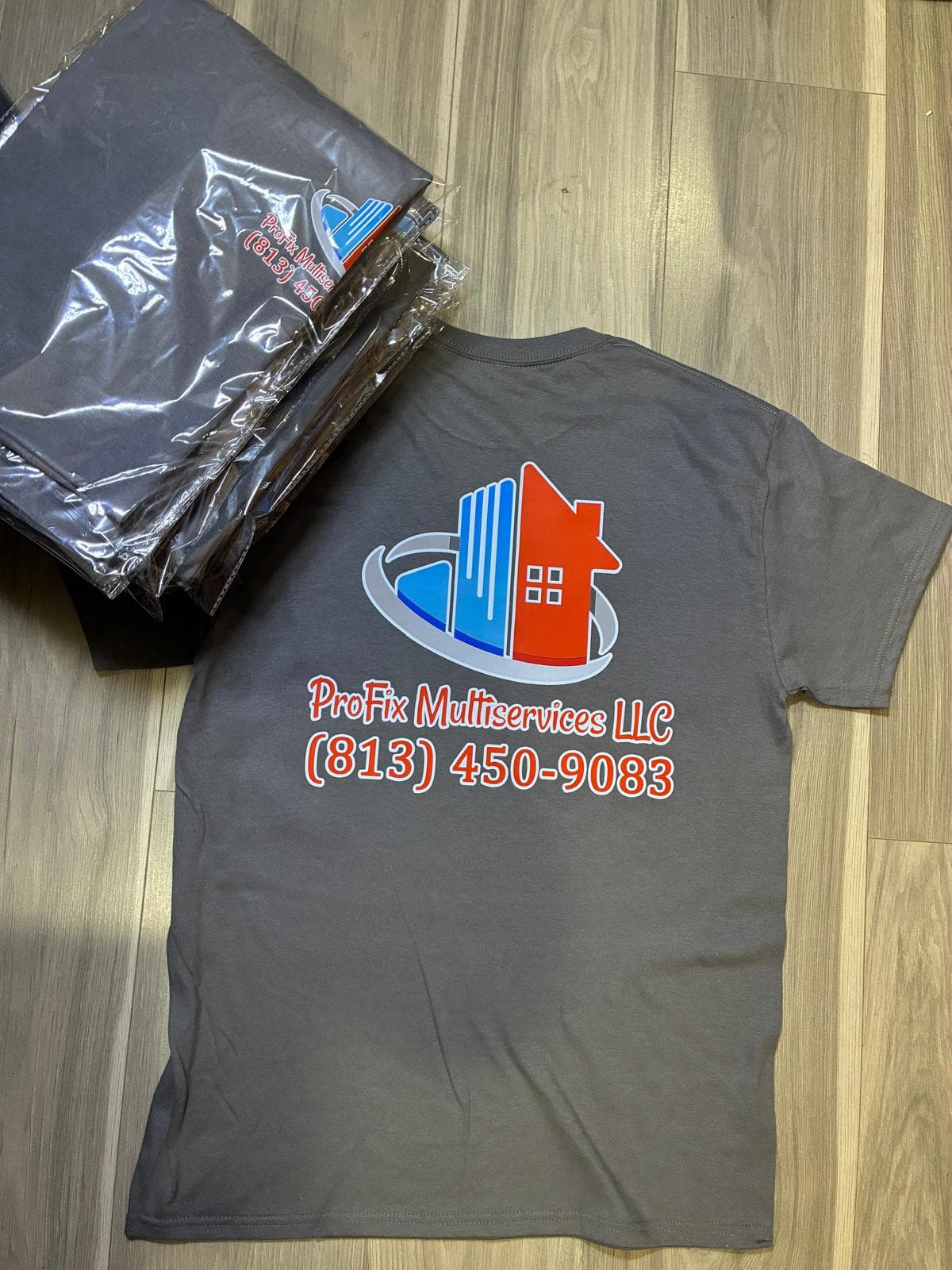 Vista trasera de camisa gris de ProFix junto a pila de camisas